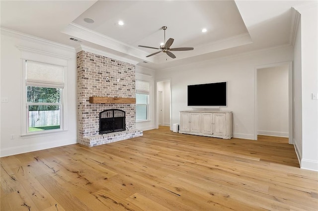 unfurnished living room with a brick fireplace, a tray ceiling, light wood-style floors, and crown molding