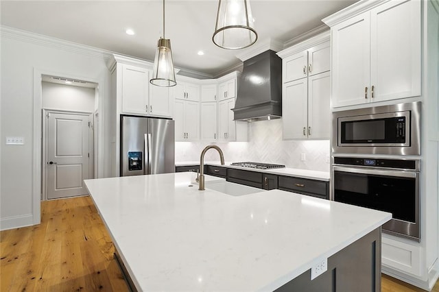 kitchen featuring a center island with sink, custom exhaust hood, light countertops, hanging light fixtures, and appliances with stainless steel finishes