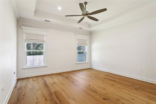 spare room featuring light wood-style floors, visible vents, a tray ceiling, and ornamental molding