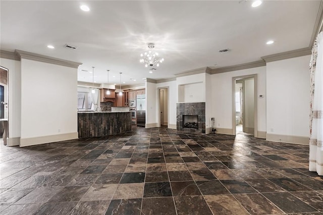 unfurnished living room featuring a tile fireplace, crown molding, and an inviting chandelier