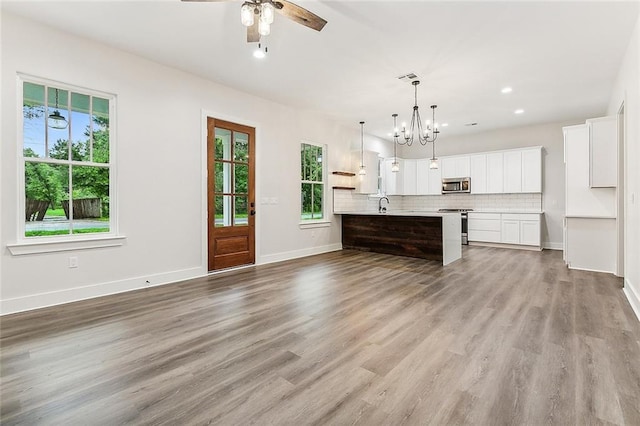 kitchen with hanging light fixtures, appliances with stainless steel finishes, white cabinets, a kitchen island with sink, and backsplash