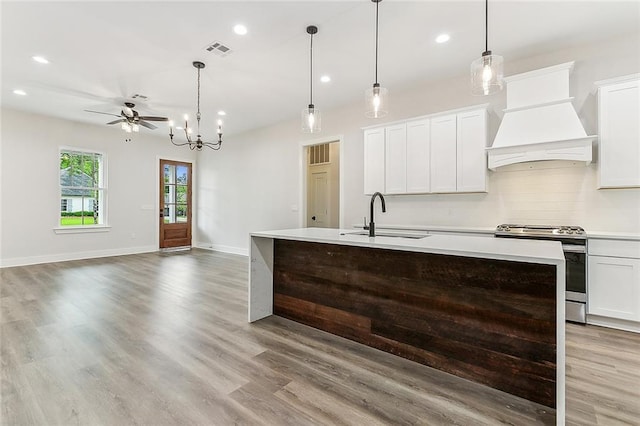 kitchen featuring stainless steel range oven, sink, custom range hood, pendant lighting, and white cabinets