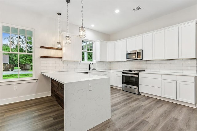 kitchen featuring appliances with stainless steel finishes, tasteful backsplash, white cabinetry, hanging light fixtures, and kitchen peninsula