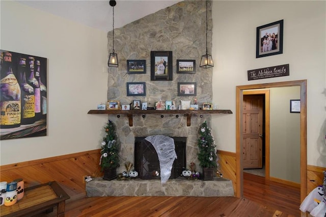 living room with a stone fireplace, wood-type flooring, vaulted ceiling, and wood walls