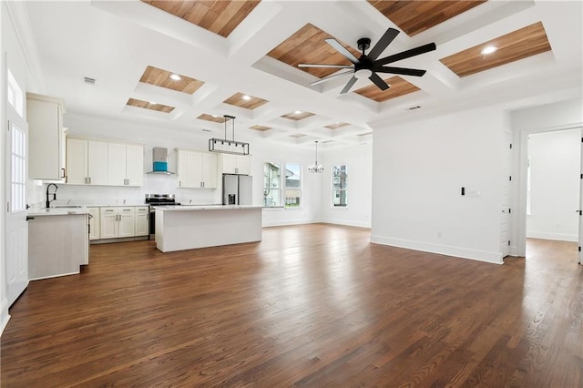 unfurnished living room with beam ceiling, plenty of natural light, ceiling fan with notable chandelier, and dark hardwood / wood-style flooring