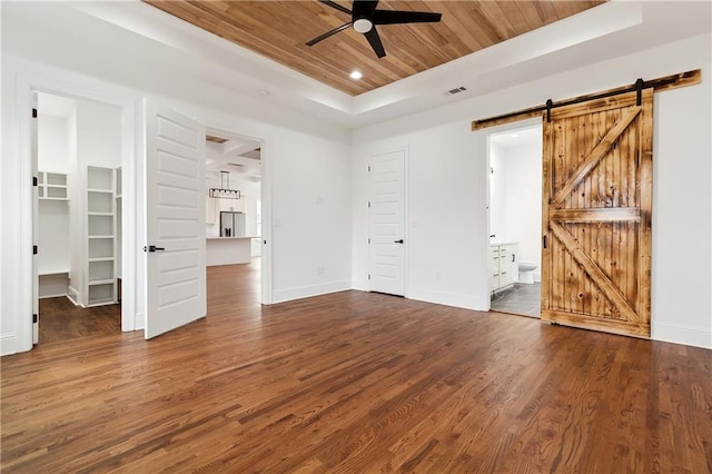 unfurnished bedroom featuring a walk in closet, a barn door, ensuite bath, ceiling fan, and dark hardwood / wood-style floors