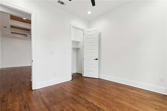 unfurnished bedroom featuring a closet, beamed ceiling, dark wood-type flooring, a spacious closet, and ceiling fan