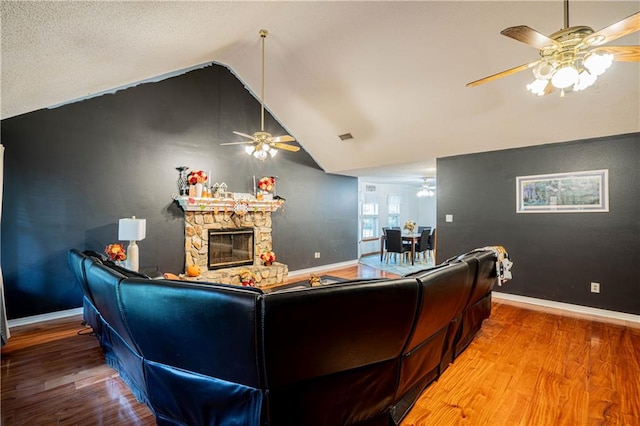 living room with lofted ceiling, a stone fireplace, hardwood / wood-style flooring, and ceiling fan