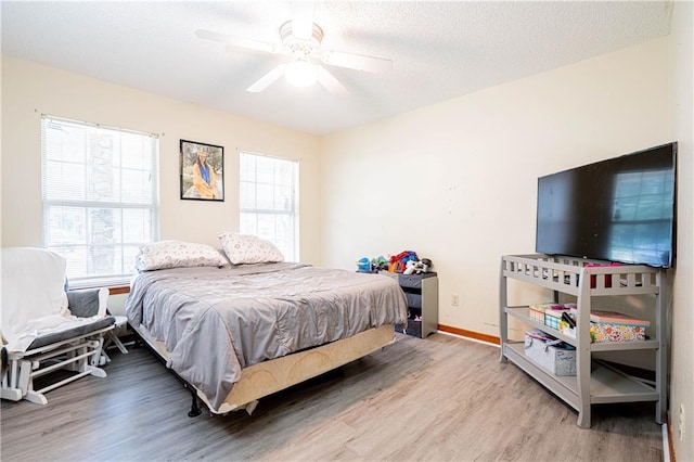 bedroom featuring ceiling fan, a textured ceiling, wood-type flooring, and multiple windows