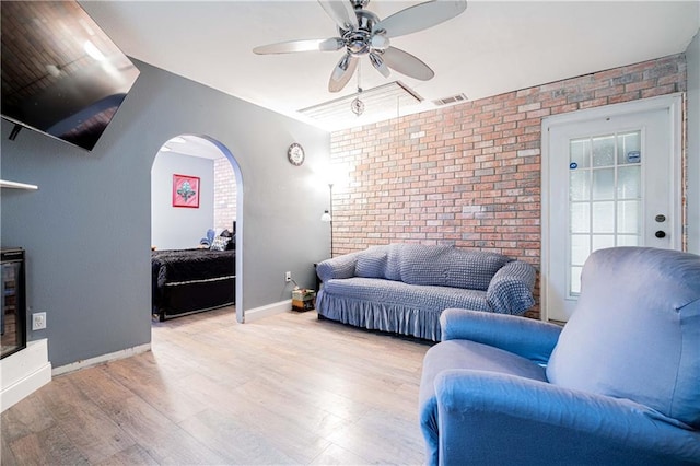 living room with ceiling fan, brick wall, and light hardwood / wood-style flooring