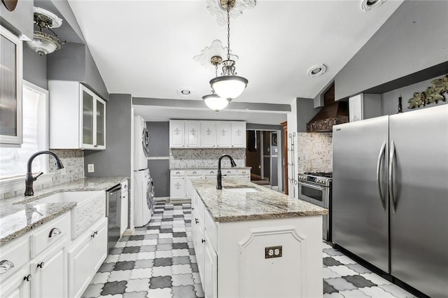 kitchen with white cabinetry, stainless steel appliances, an island with sink, and stacked washer and clothes dryer