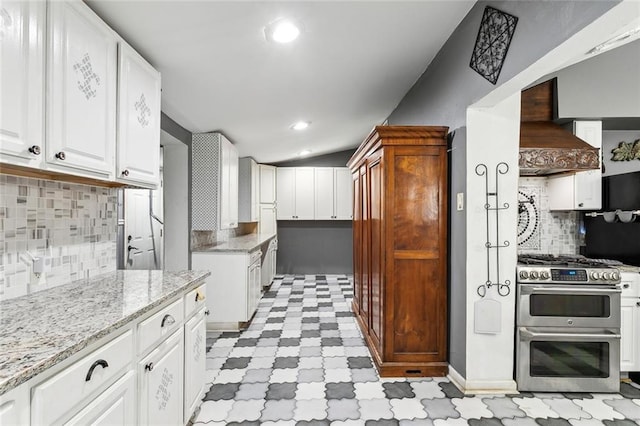 kitchen featuring tasteful backsplash, white cabinetry, custom range hood, range with two ovens, and light stone counters