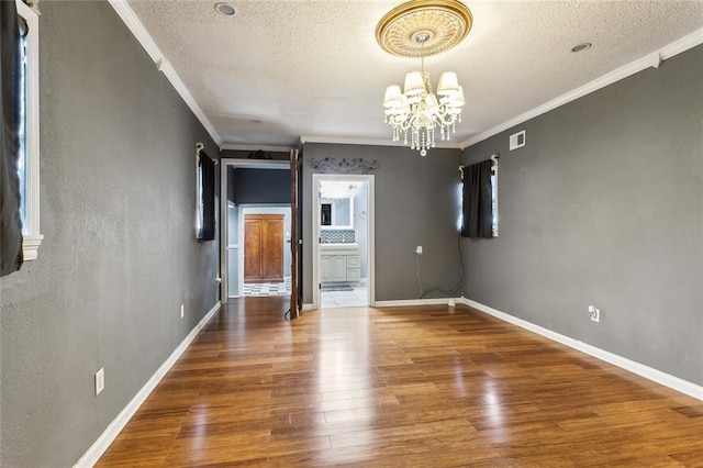 empty room featuring crown molding, a textured ceiling, a chandelier, and wood-type flooring