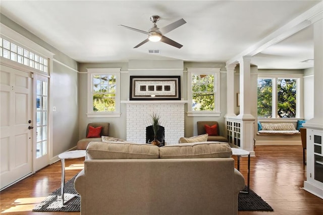 living room with dark hardwood / wood-style flooring, decorative columns, ceiling fan, and a brick fireplace