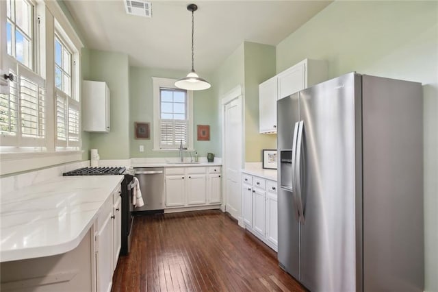 kitchen with stainless steel appliances, decorative light fixtures, dark hardwood / wood-style floors, light stone countertops, and white cabinets