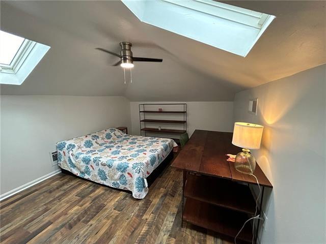 bedroom with dark wood-type flooring, ceiling fan, and vaulted ceiling with skylight