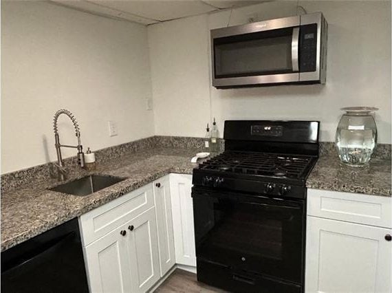 kitchen featuring black appliances, white cabinetry, stone counters, and sink