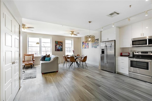 kitchen with stainless steel appliances, tasteful backsplash, ceiling fan, white cabinetry, and light hardwood / wood-style flooring