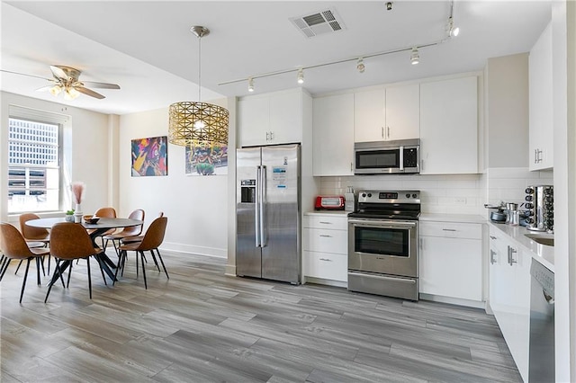 kitchen featuring white cabinetry, appliances with stainless steel finishes, hanging light fixtures, decorative backsplash, and ceiling fan