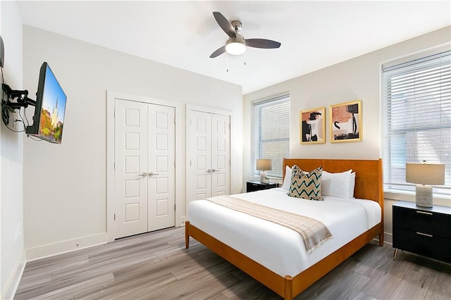 bedroom featuring multiple closets, multiple windows, hardwood / wood-style floors, and ceiling fan