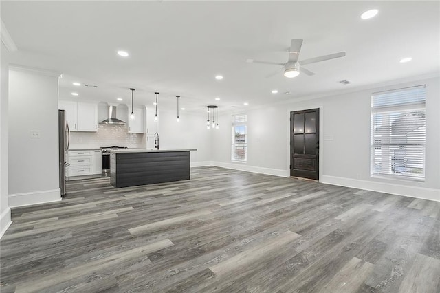 kitchen with a kitchen island with sink, wall chimney range hood, stainless steel appliances, pendant lighting, and white cabinetry