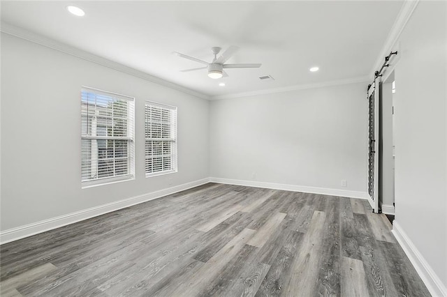 spare room with ceiling fan, crown molding, wood-type flooring, and a barn door