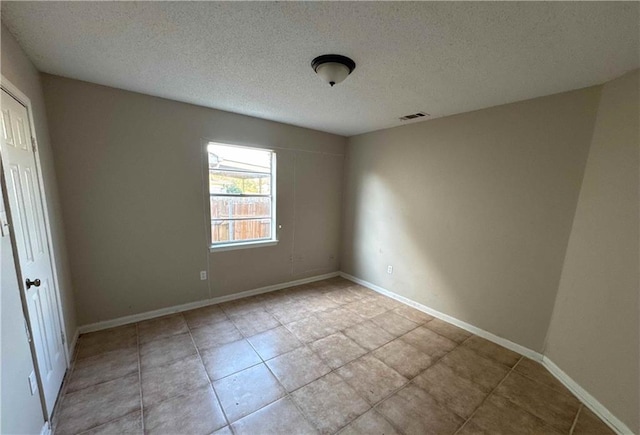 tiled empty room featuring a textured ceiling