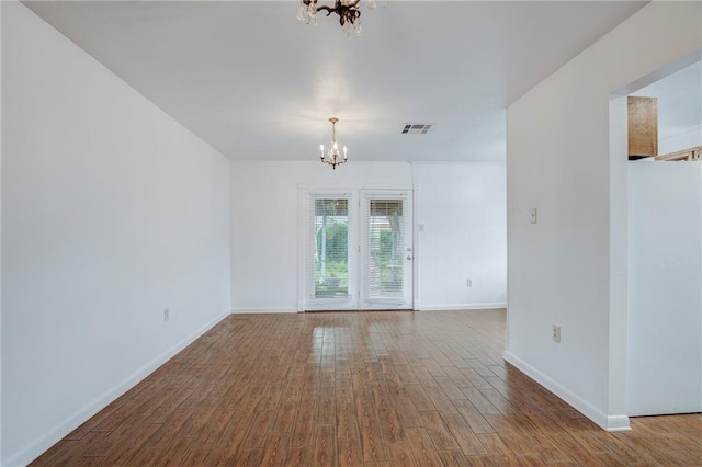 spare room with hardwood / wood-style flooring and an inviting chandelier