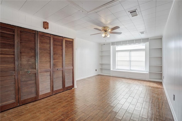 unfurnished bedroom featuring hardwood / wood-style floors, ceiling fan, and wooden walls