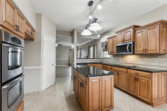 kitchen featuring dark stone counters, stainless steel appliances, sink, pendant lighting, and a center island