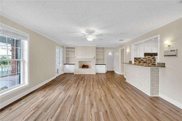 unfurnished living room featuring light hardwood / wood-style floors, built in features, a healthy amount of sunlight, and crown molding