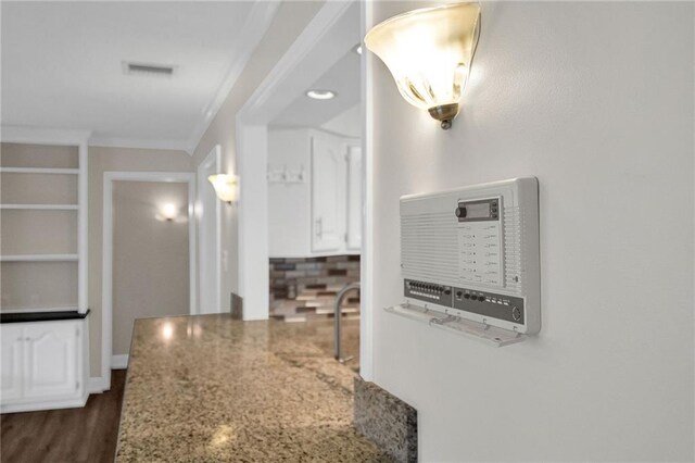 interior details featuring light stone countertops, crown molding, and dark wood-type flooring