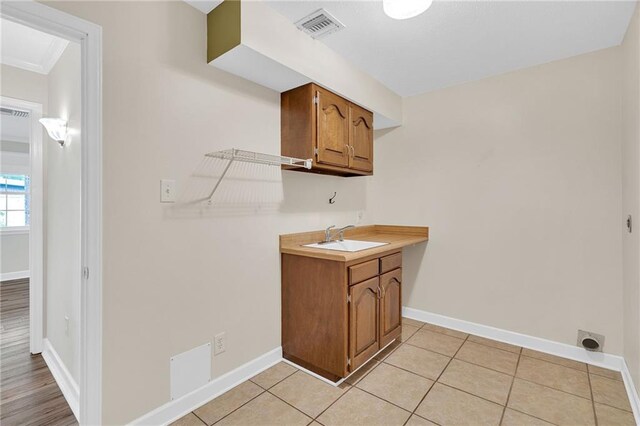 clothes washing area featuring light tile patterned flooring, crown molding, and sink