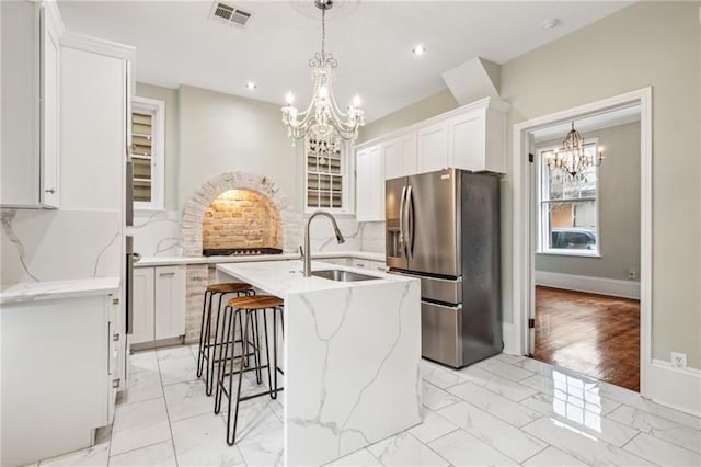 kitchen featuring stainless steel fridge, decorative backsplash, an island with sink, light hardwood / wood-style floors, and white cabinets