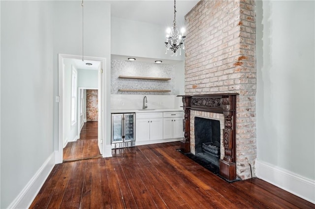 unfurnished living room featuring a towering ceiling, wine cooler, dark hardwood / wood-style flooring, wet bar, and a brick fireplace