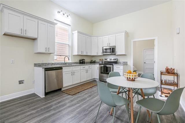 kitchen featuring white cabinets, light stone counters, wood-type flooring, and stainless steel appliances