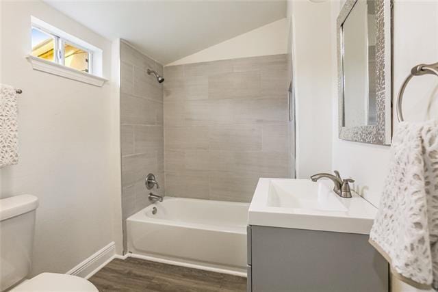 full bathroom with tiled shower / bath combo, wood-type flooring, vaulted ceiling, toilet, and vanity