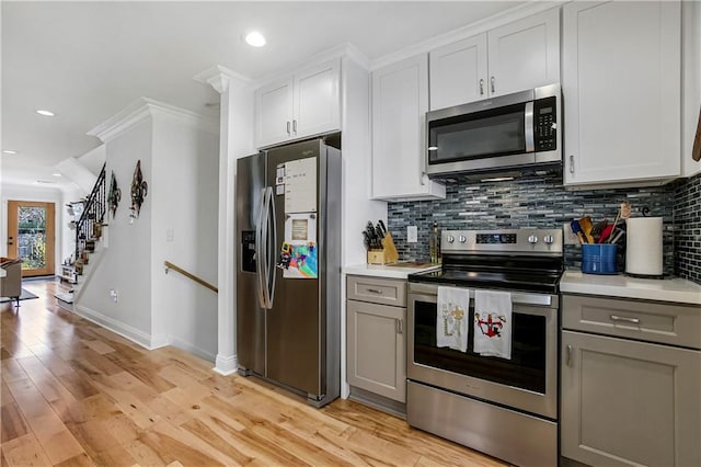 kitchen with ornamental molding, white cabinetry, appliances with stainless steel finishes, gray cabinets, and light hardwood / wood-style floors