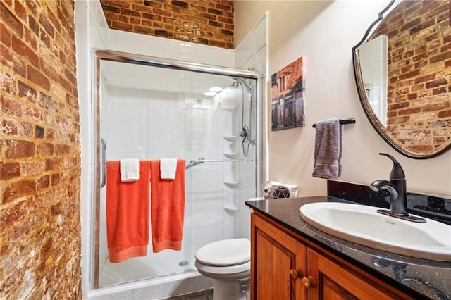 bathroom featuring vanity, toilet, a shower with door, and brick wall