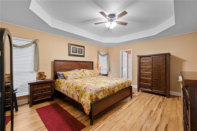 bedroom featuring light wood-type flooring, ceiling fan, and a raised ceiling