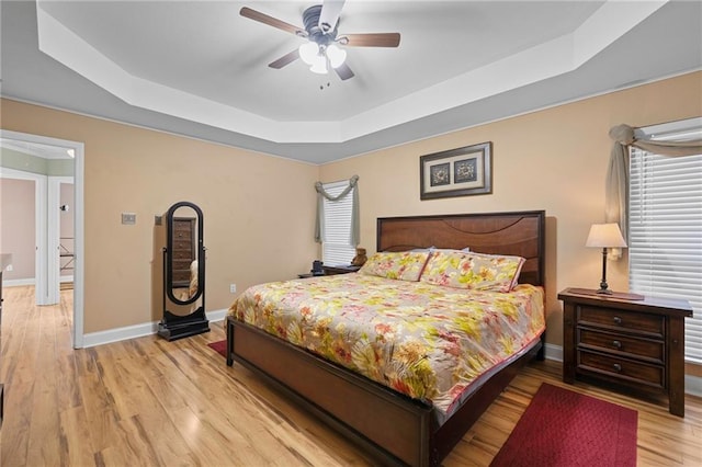 bedroom with ceiling fan, light wood-type flooring, and a tray ceiling