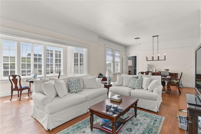 living room with a wealth of natural light, an inviting chandelier, and light hardwood / wood-style flooring