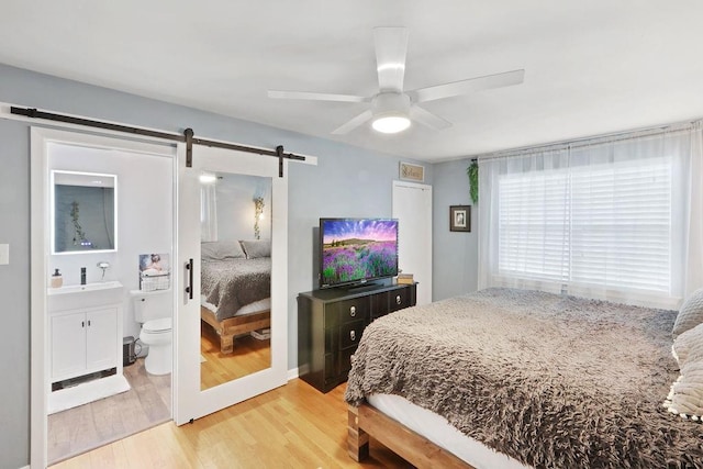 bedroom with ensuite bathroom, ceiling fan, sink, a barn door, and light hardwood / wood-style flooring