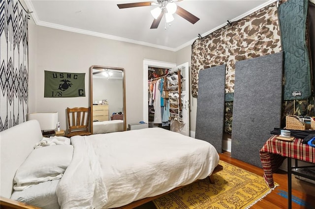 bedroom featuring a closet, a spacious closet, wood-type flooring, crown molding, and ceiling fan