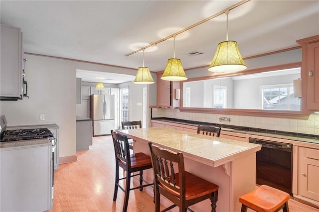 kitchen with light hardwood / wood-style flooring, a breakfast bar area, appliances with stainless steel finishes, decorative backsplash, and decorative light fixtures