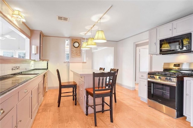 kitchen featuring a kitchen bar, sink, gas range, white cabinetry, and hanging light fixtures