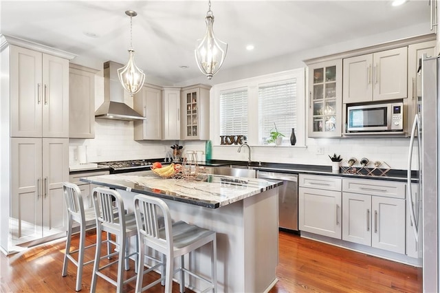 kitchen featuring appliances with stainless steel finishes, hardwood / wood-style floors, a kitchen island, wall chimney range hood, and pendant lighting