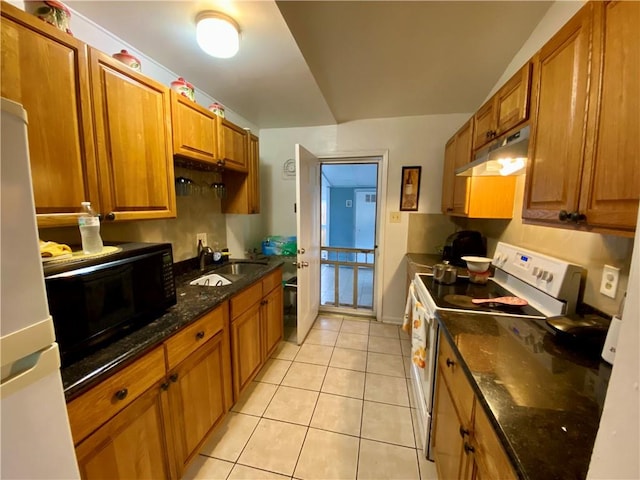 kitchen with light tile patterned floors, white appliances, dark stone countertops, and sink