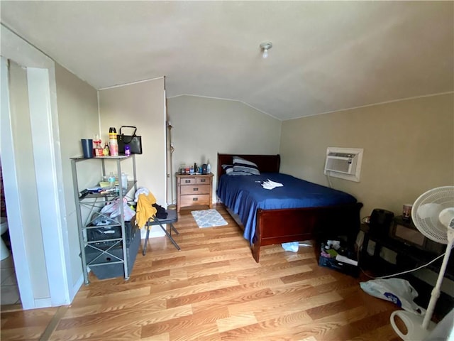 bedroom with lofted ceiling, a wall unit AC, and light hardwood / wood-style flooring