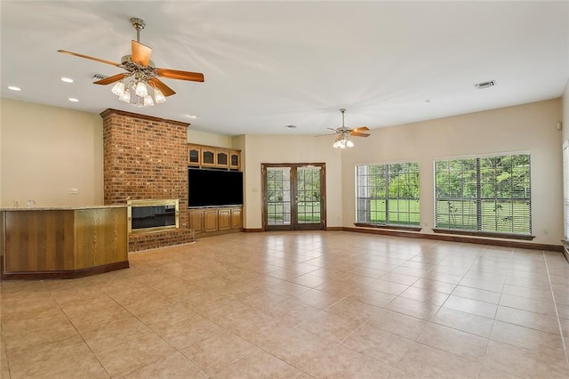 unfurnished living room with a brick fireplace, french doors, ceiling fan, and light tile patterned floors